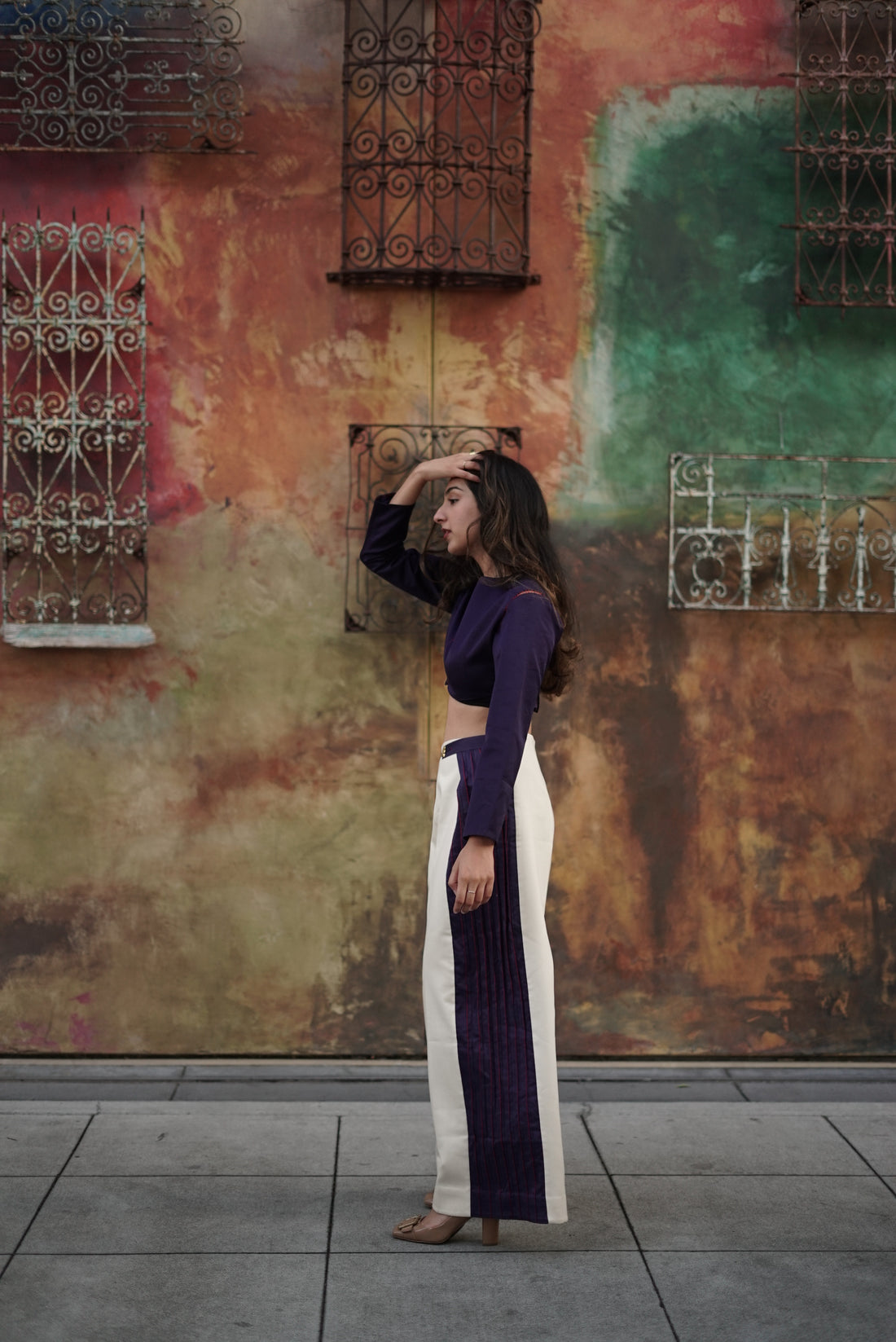 Aditi Mayer wearing a dress and heels in front of a colourful outdoor wall