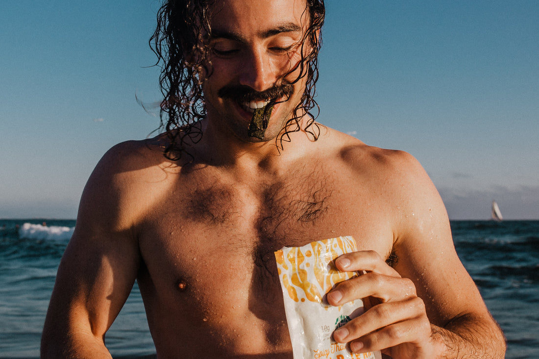 topless man on a beach eating some kelp jerky
