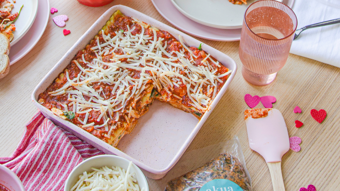 Dish of lasagna with pink crockery, utensils, drink and heart confetti on the table
