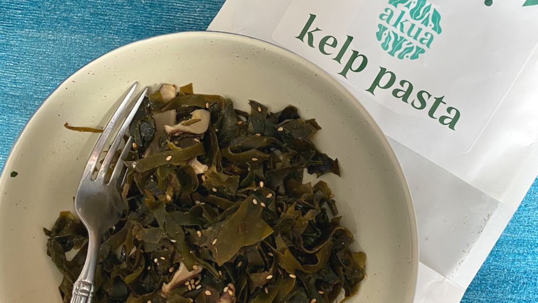 Bowl of kelp pasta with sesame seeds and mushrooms, sitting on top of a kelp pasta packet