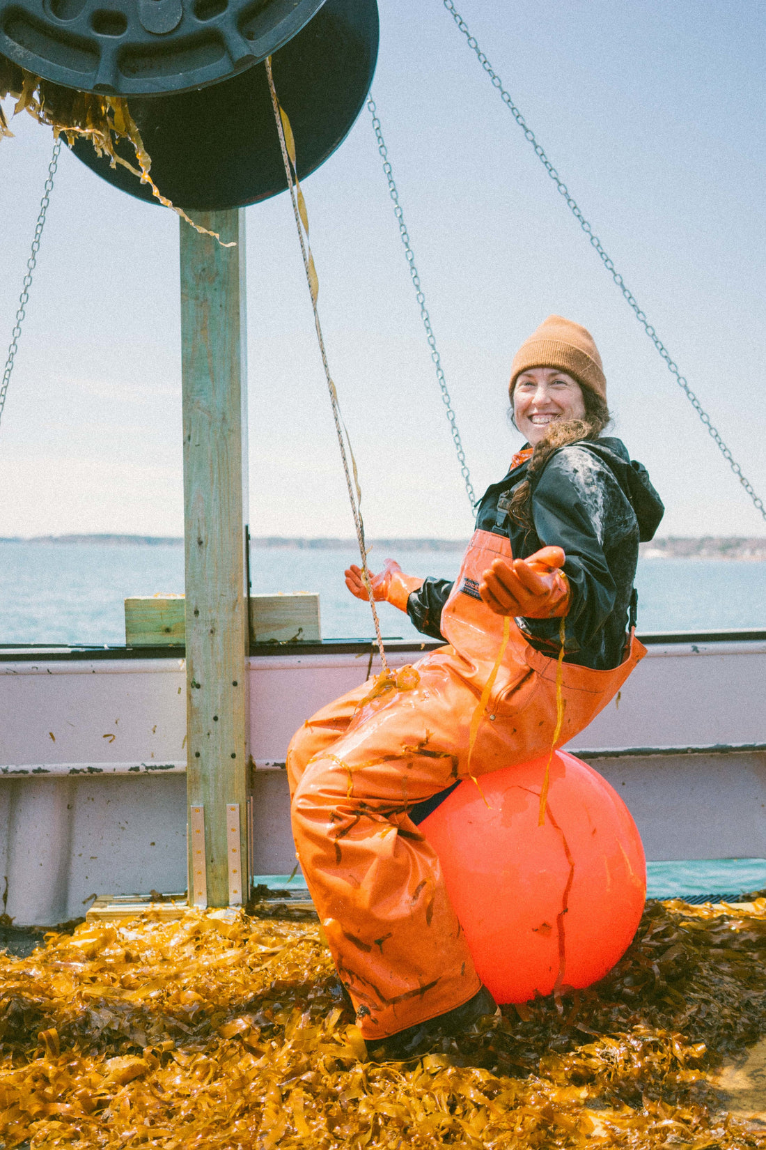 Colleen smiling, sitting on a big buoy on top of a pile of kelp